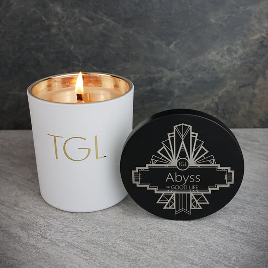 White candle with gold interior and black lid labeled 'Abyss' on a gray surface with dark background