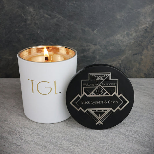 White candle with gold interior and black coaster on a gray surface against a dark background