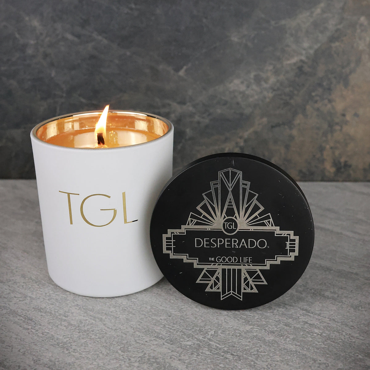 Candle with 'TGL' branding and a black coaster with 'Desperado' branding on a gray surface.