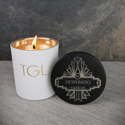 Candle with 'TGL' branding and a black coaster with 'Desperado' branding on a gray surface.