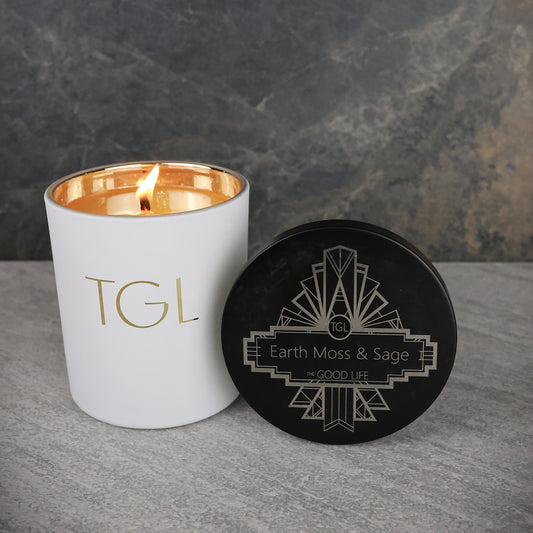 White candle with gold interior and black lid on a gray surface with a dark background