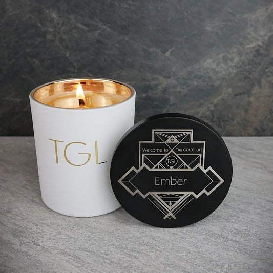 White candle with gold interior and black coaster on a gray surface against a dark background