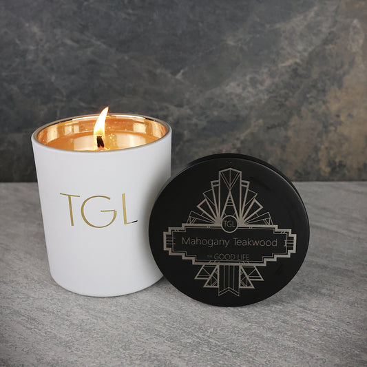 White candle with gold interior and black lid featuring 'TGL' branding on a gray surface.