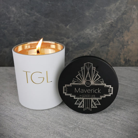 Candle with 'TGL' branding and a coaster with 'Maverick' branding on a gray surface.