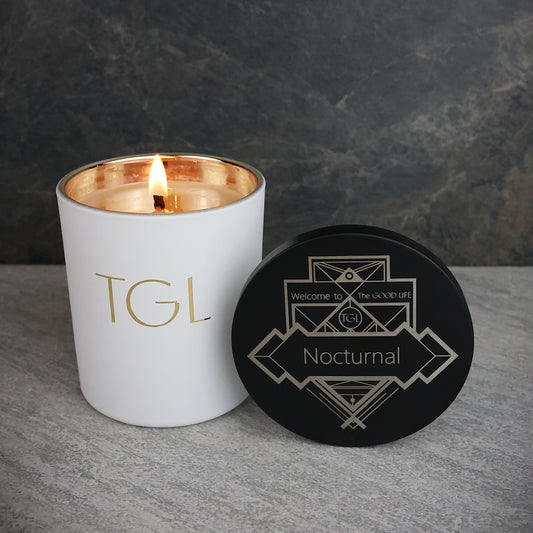 White candle with gold interior and black coaster on a gray surface against a dark background