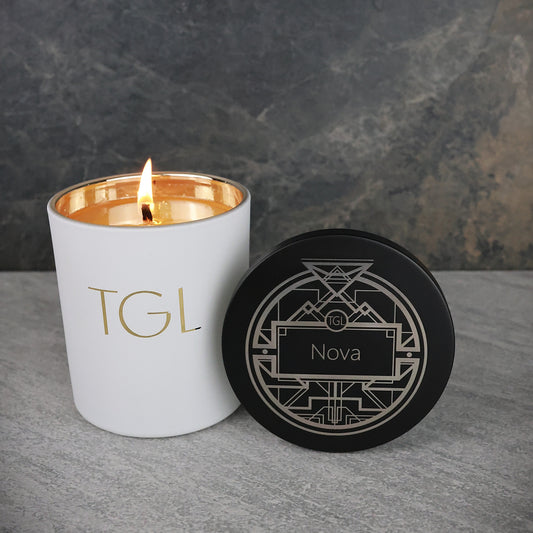 White candle with gold interior and black lid labeled 'Nova' on a gray surface.