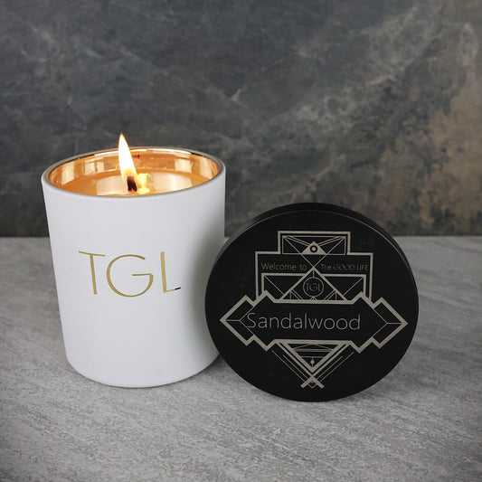 Candle with 'TGL' branding and a black coaster with 'Sandalwood' text on a gray surface.