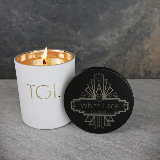 Candle with 'TGL' branding and a black coaster labeled 'White Lace' on a gray surface.