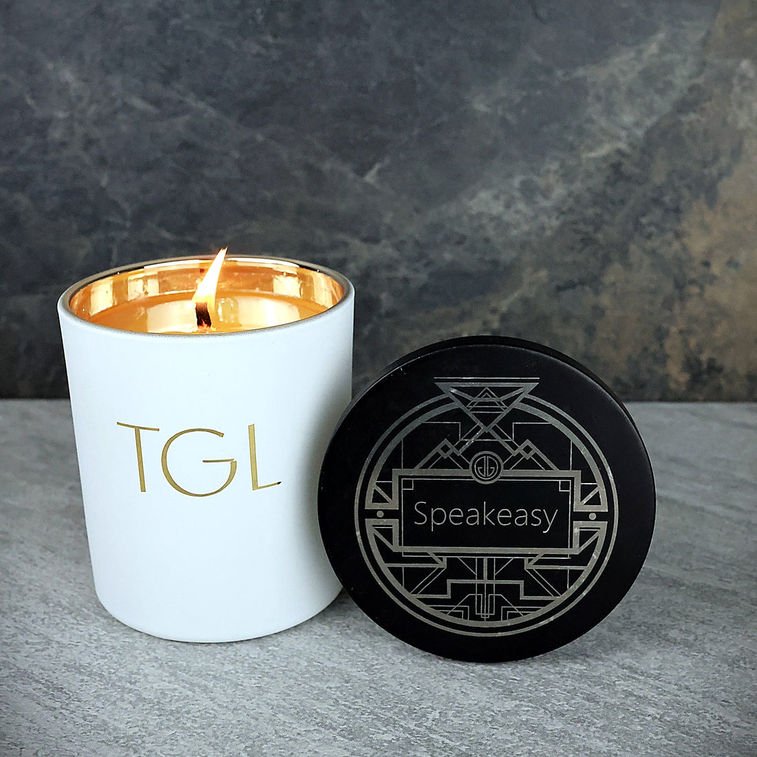 Lit Speakeasy TGL soy candle beside its black Art Deco engraved lid