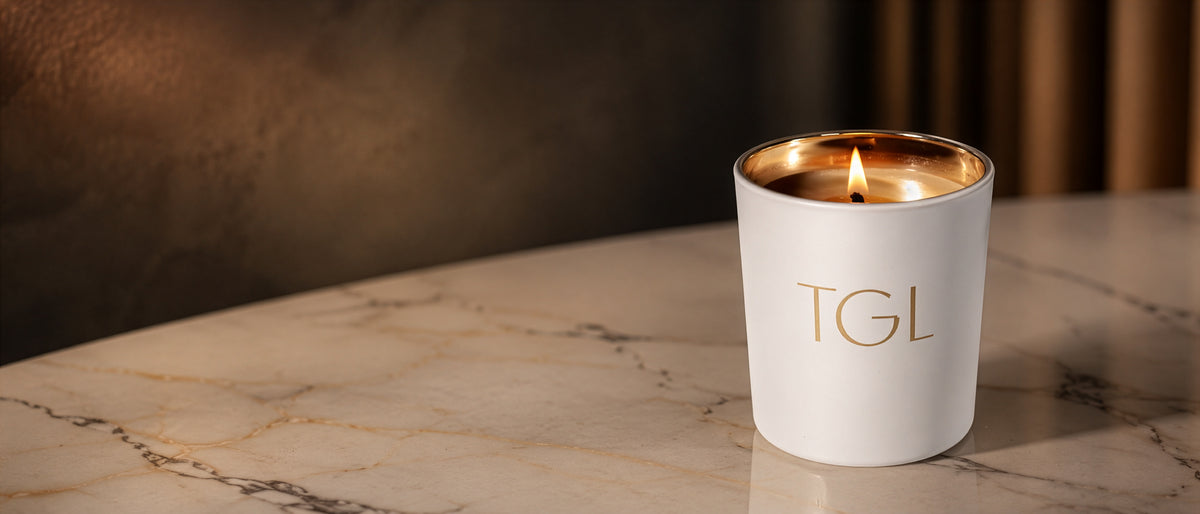 Lit white TGL candle with a gold interior on a marble tabletop in warm light.