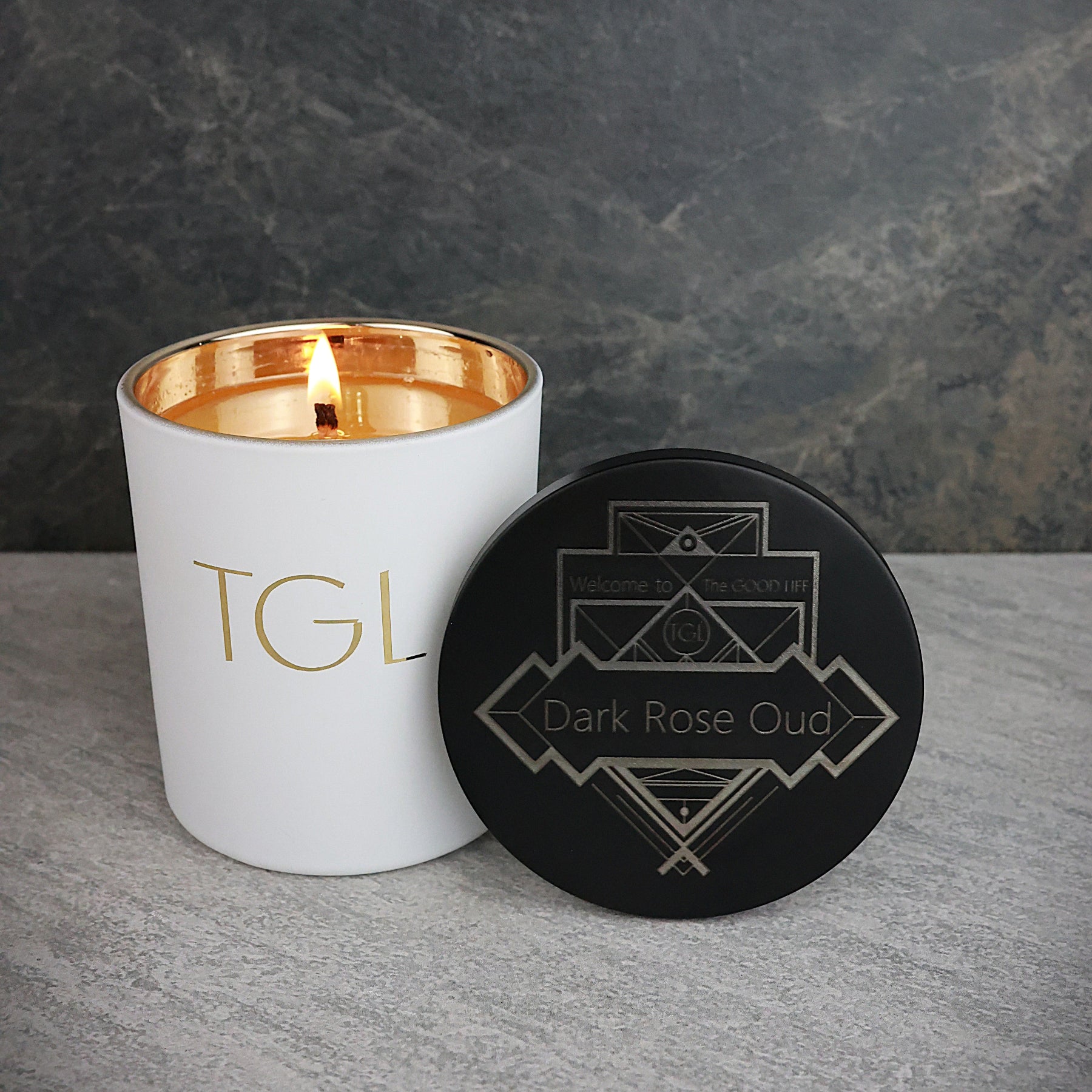 White candle with gold interior and black coaster on a gray surface