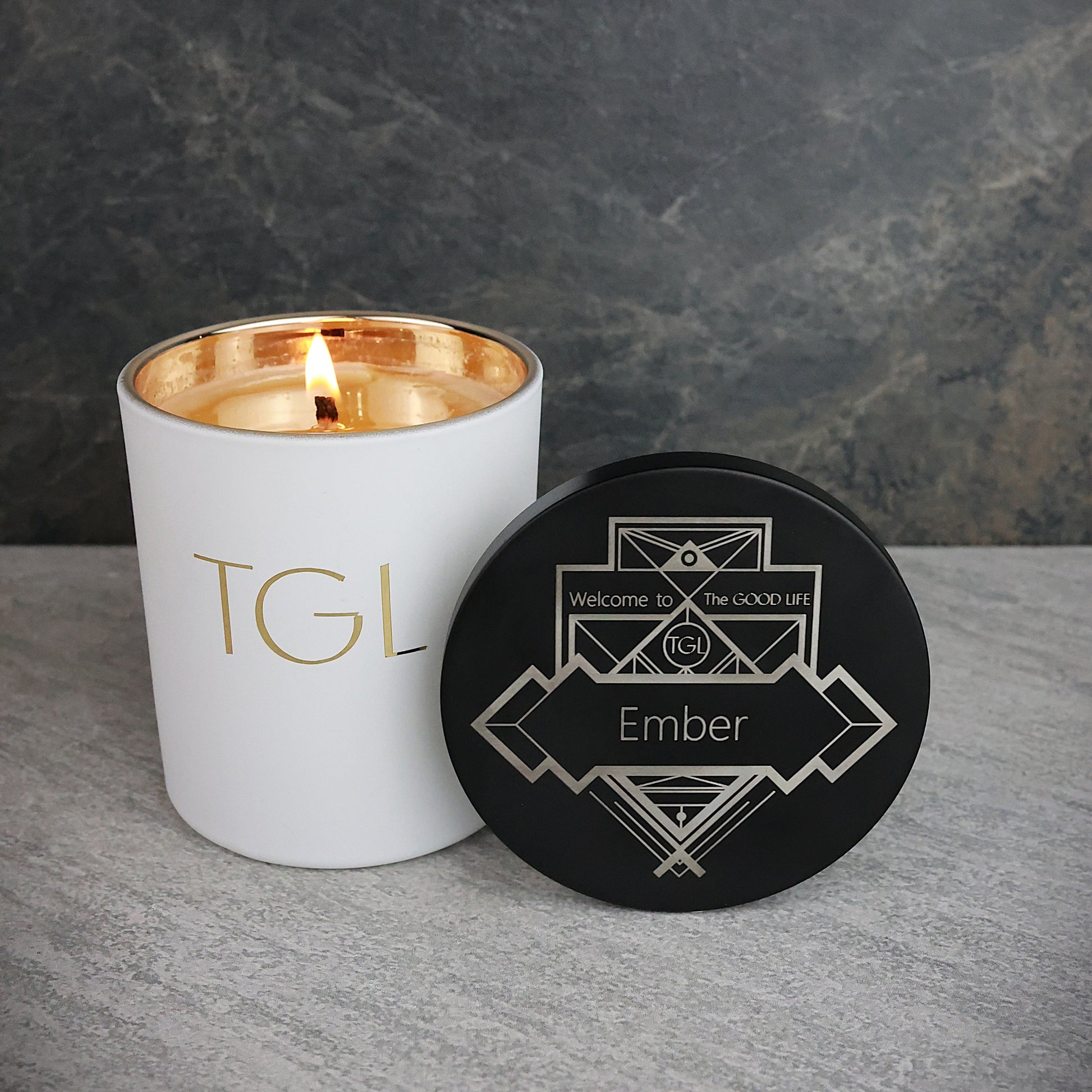 White candle with gold interior and black coaster on a gray surface against a dark background
