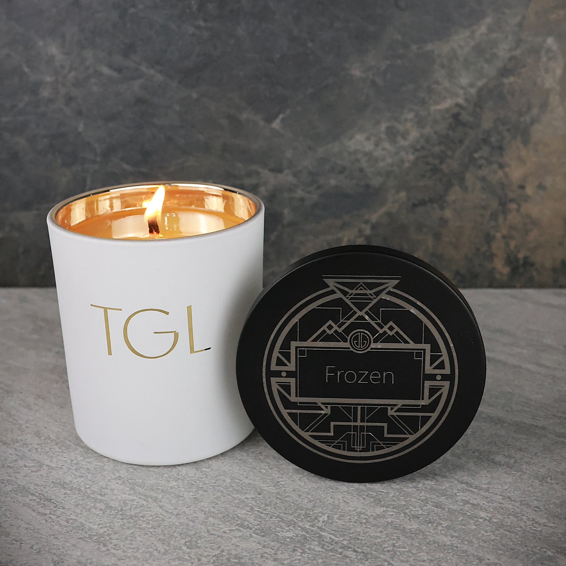 White candle with gold interior and black coaster on a gray surface