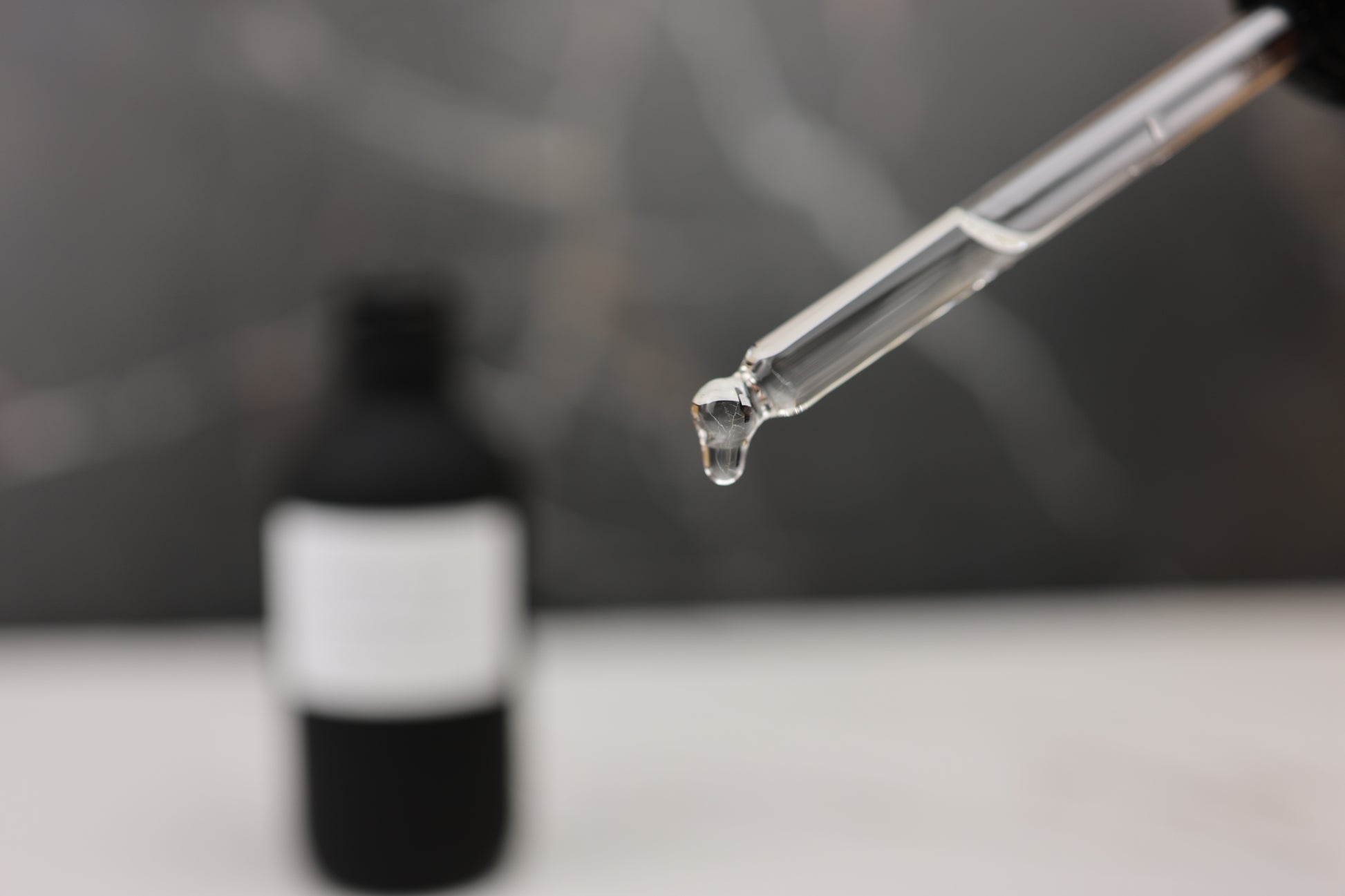 Dropper with liquid over a black bottle on a blurred background