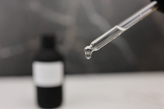 Dropper with liquid over a black bottle on a blurred background