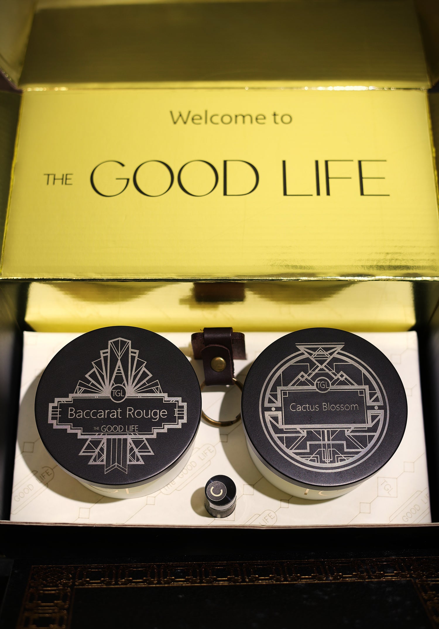 Two soy candles with laser-engraved Art Deco design. Baccarat Rouge and Cactus Blossom scent, In a gift box with gold foil and the words 'Welcome to The Good Life' .