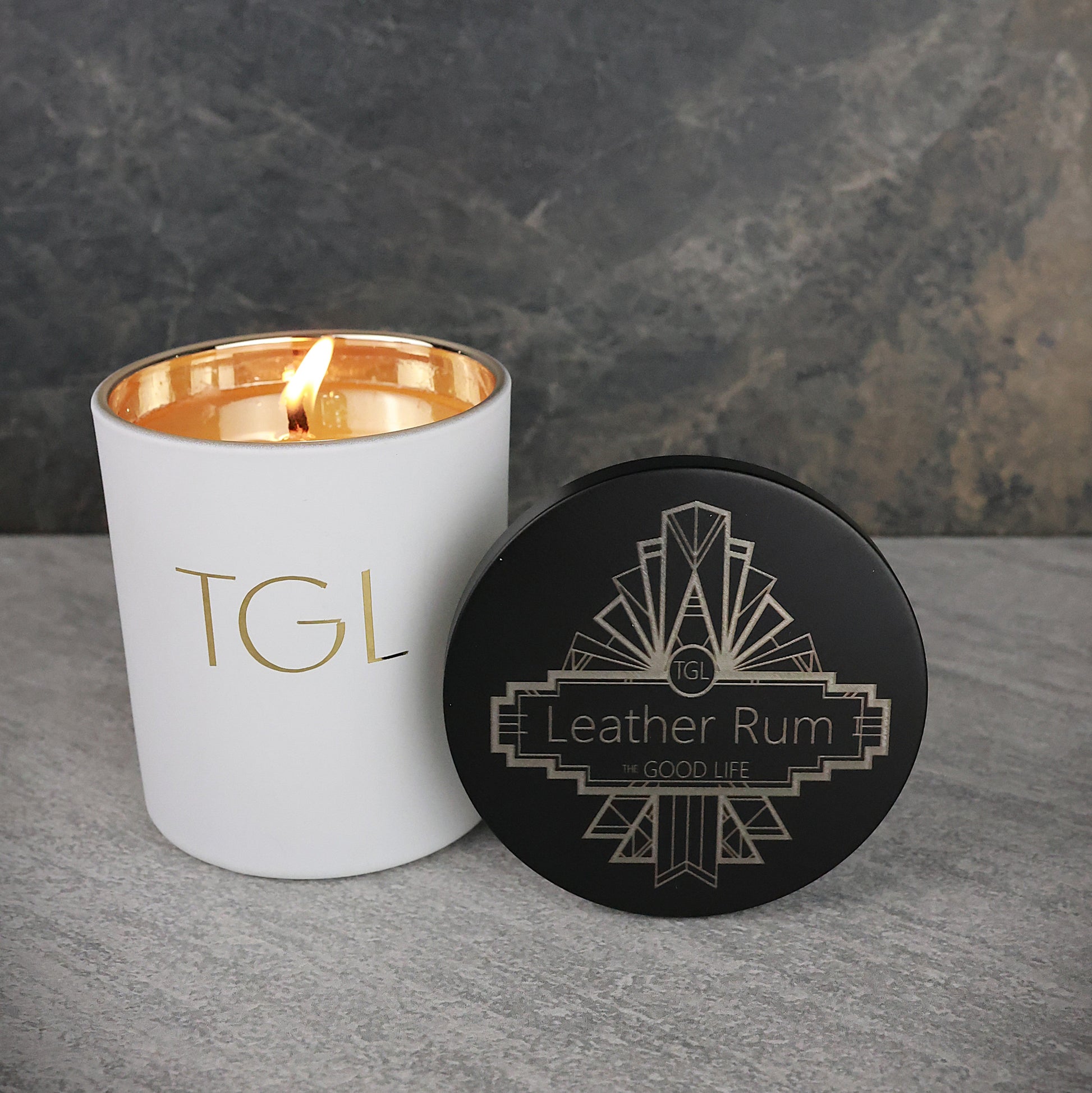 White candle with gold interior and black coaster on a gray surface