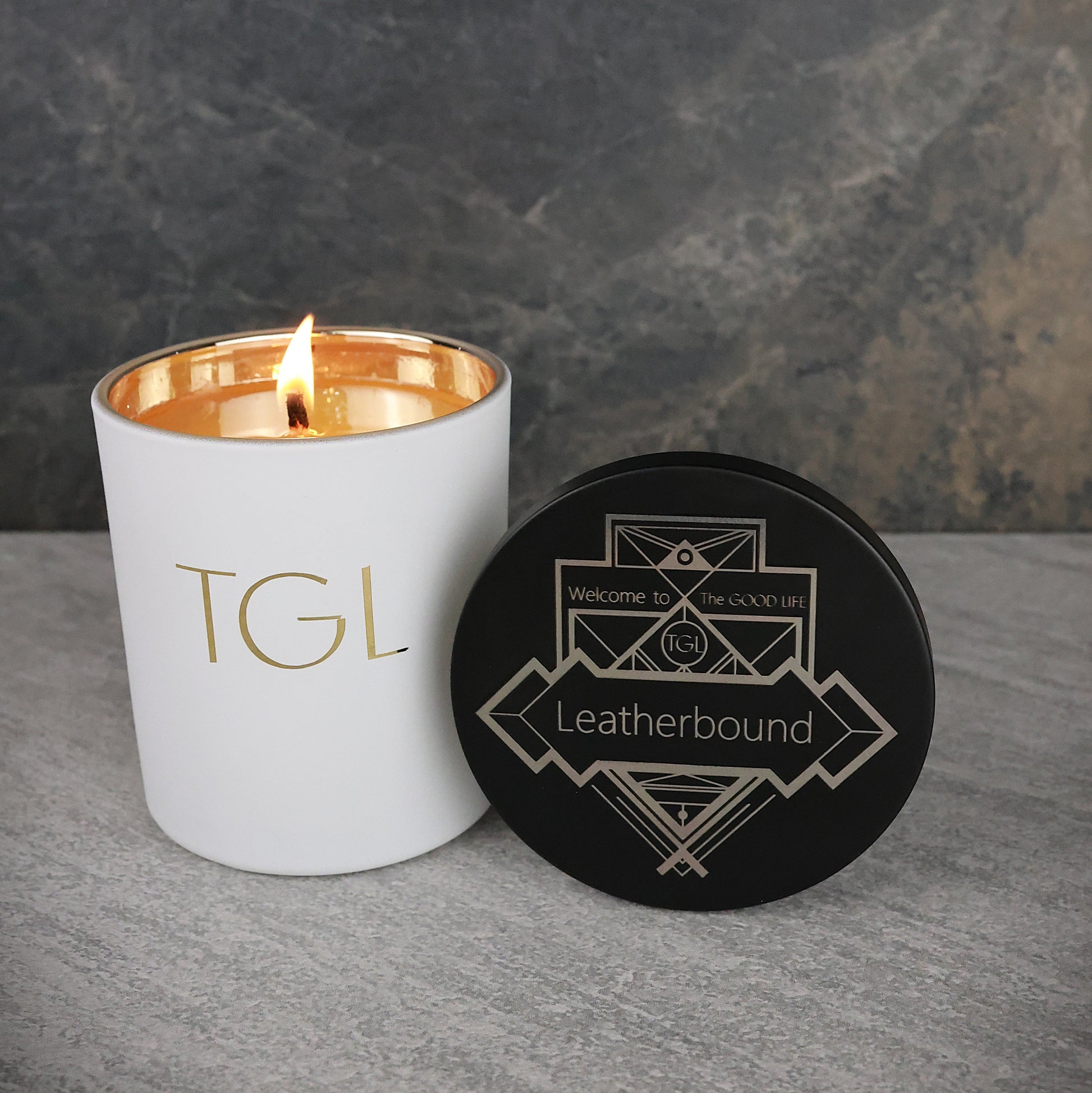 White candle with gold interior and black lid on a gray surface with a dark background