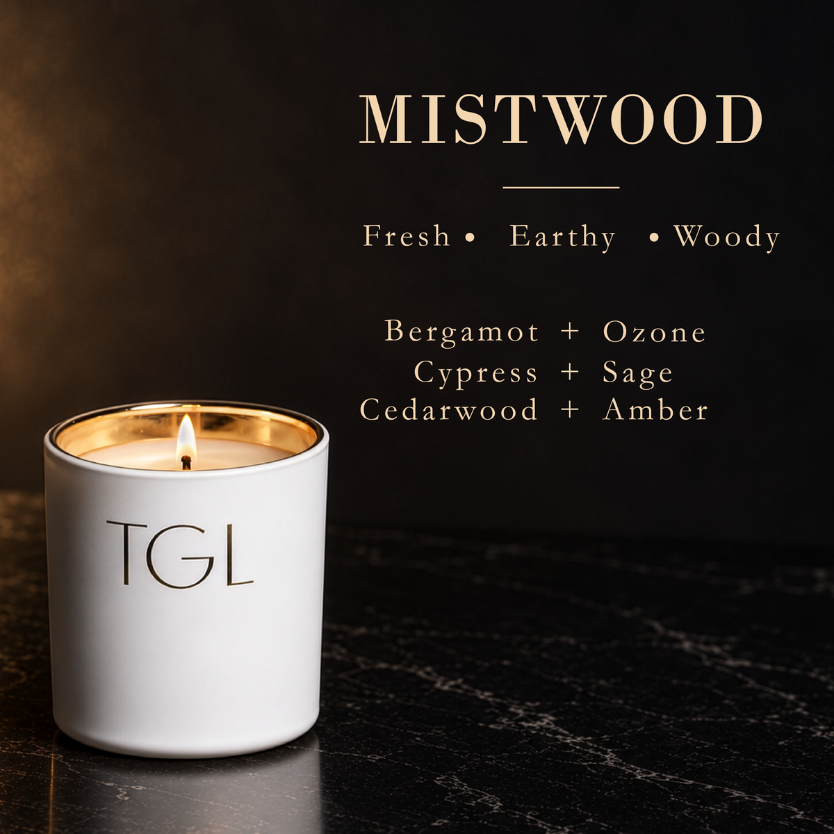 A lit TGL candle in a white ceramic jar with a gold rim sits on a dark marble surface against a dark background. Gold text at the top reads 'MISTWOOD' with scent notes 'Fresh • Earthy • Woody' and ingredient combinations below.