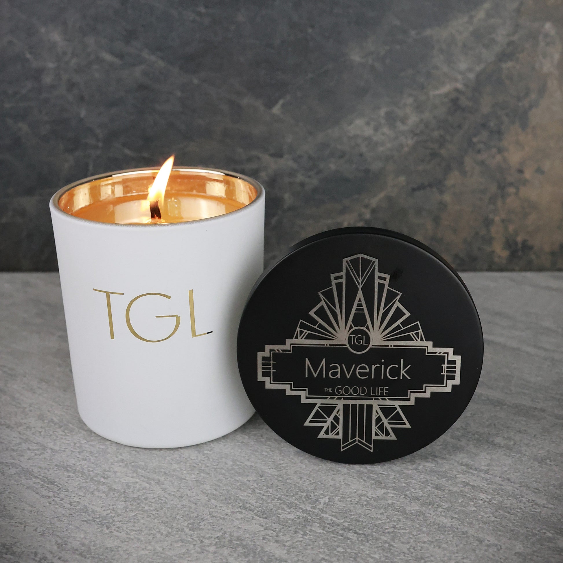 Candle with 'TGL' branding and a coaster with 'Maverick' branding on a gray surface.