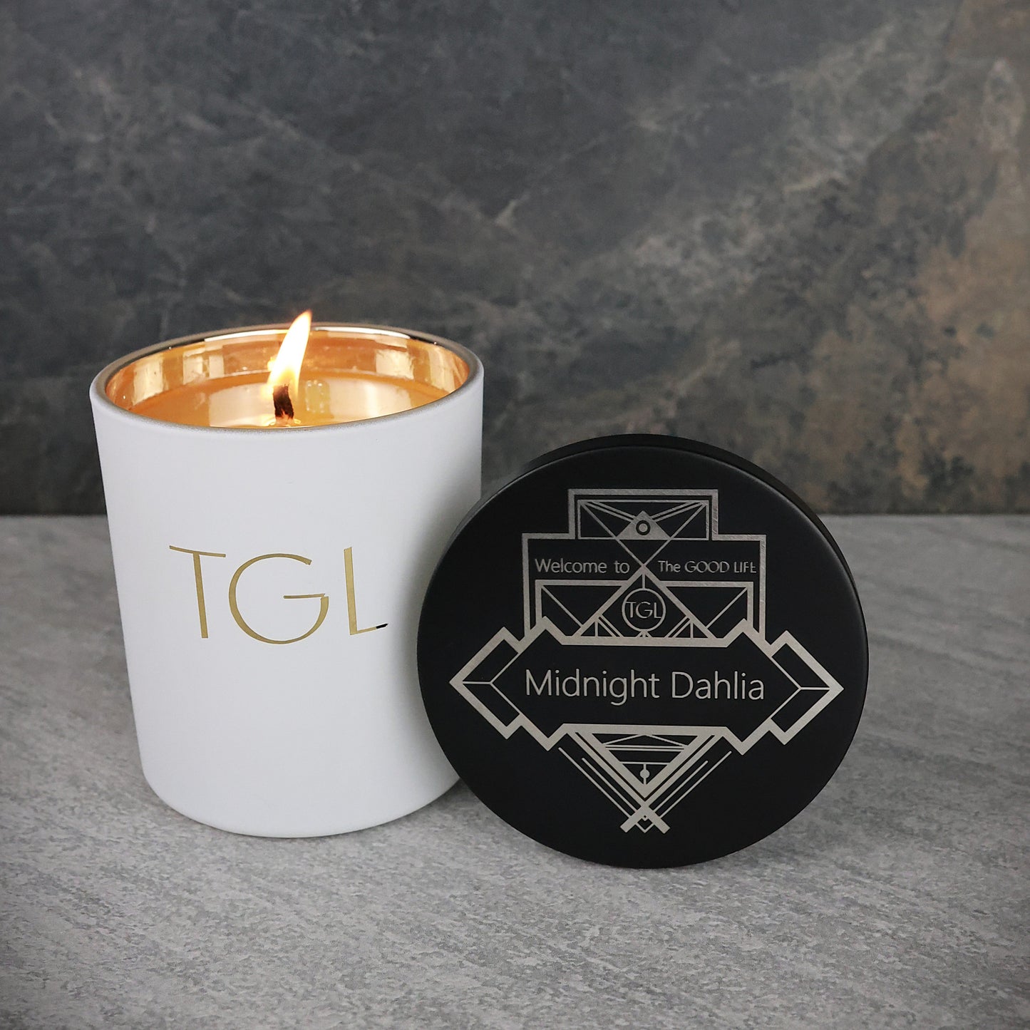 White candle with gold interior and black coaster on a gray surface