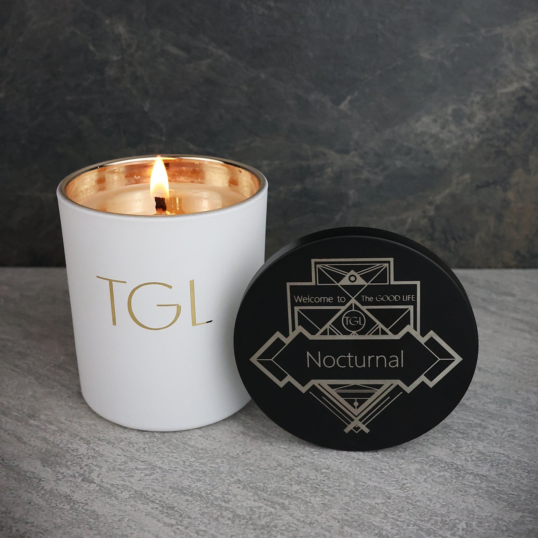 White candle with gold interior and black coaster on a gray surface against a dark background