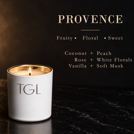 A white TGL candle with a gold-washed rim and a lit flame, set on a dark marble surface against a dark background with gold text reading 'NOCTURNAL' and scent notes.