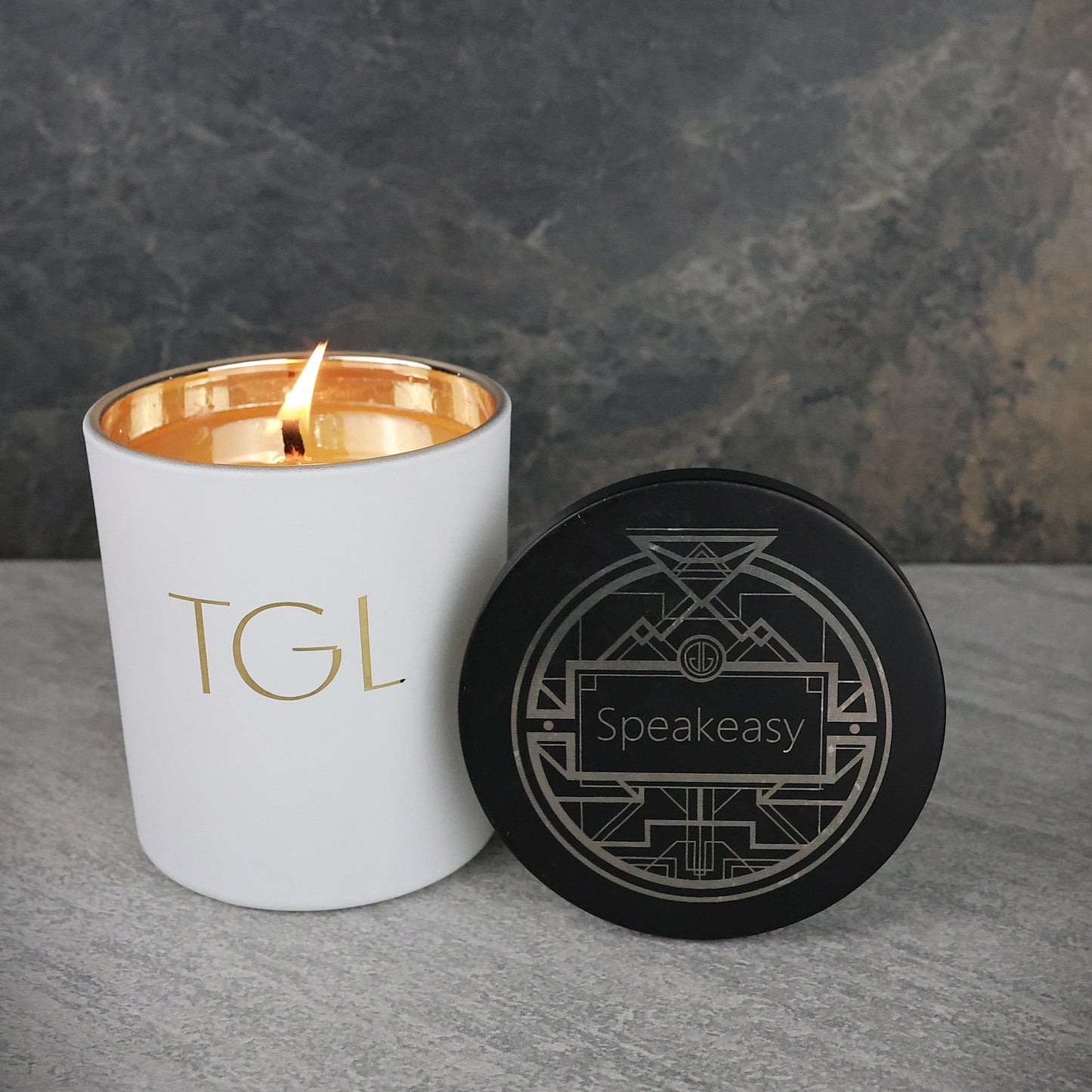 White candle with gold interior and black coaster on a gray surface
