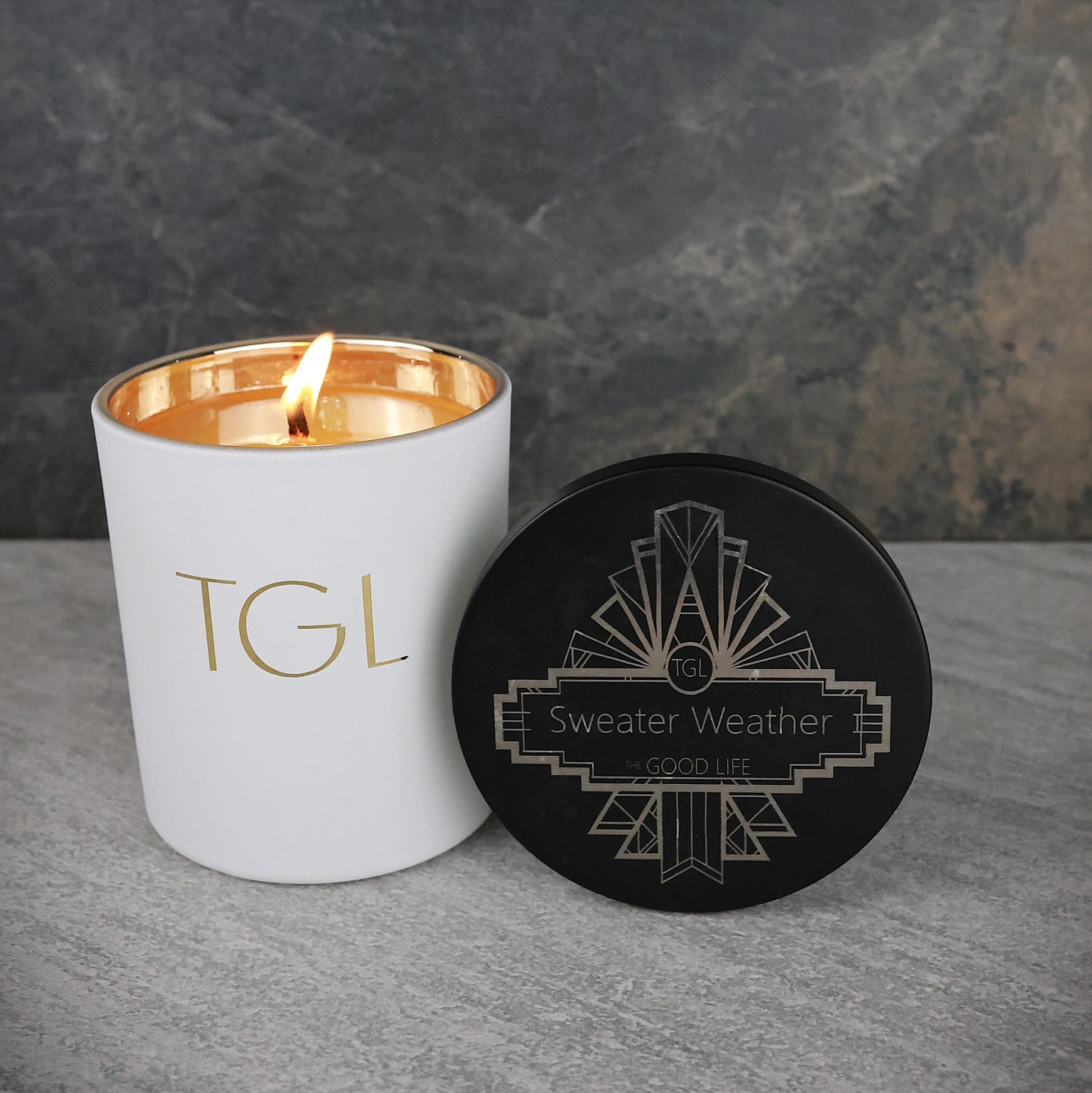 White candle with gold interior and black coaster on a gray surface