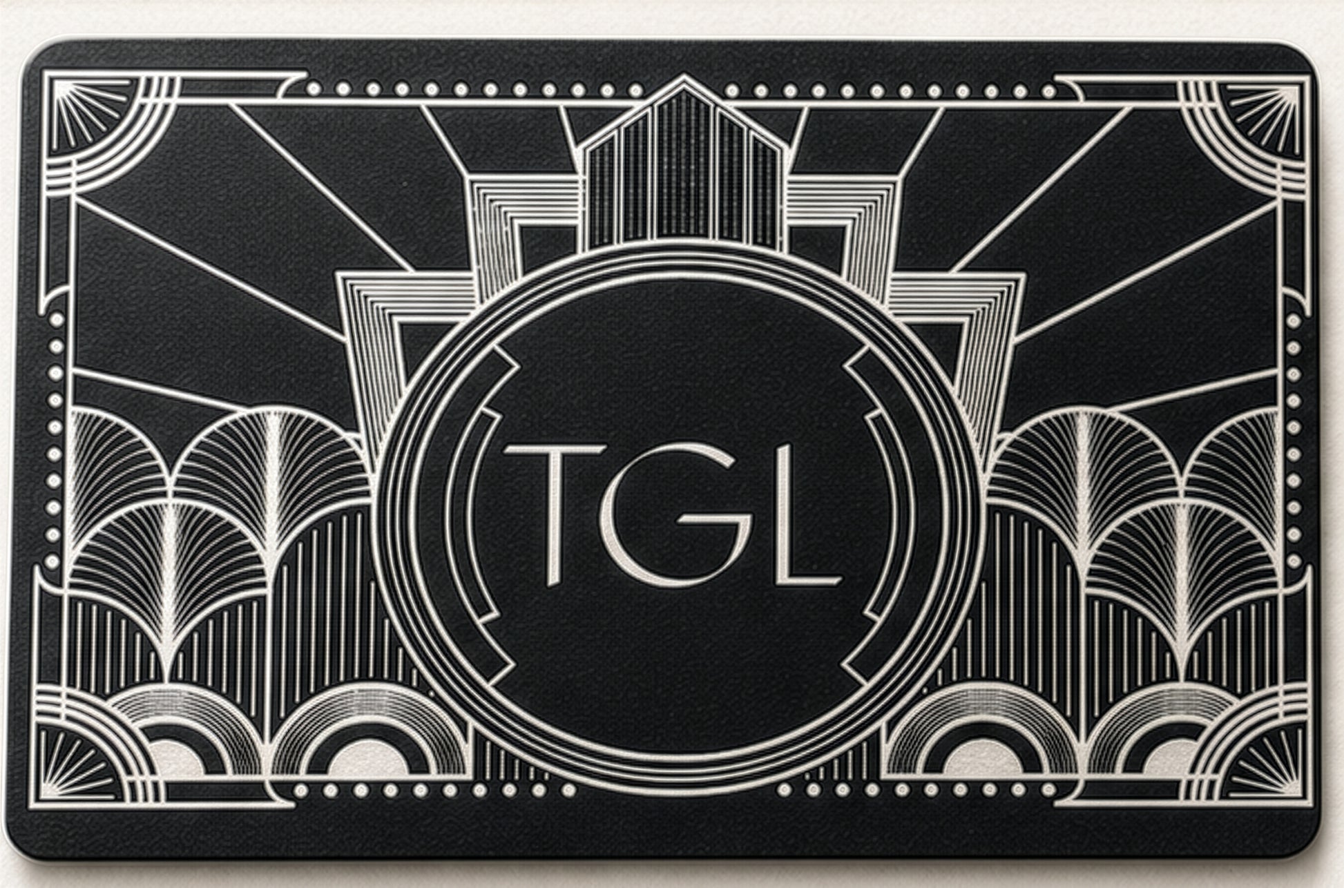 A black rectangular card or mat featuring an Art Deco style white line design with the letters 'TGL' centered inside a circular emblem.