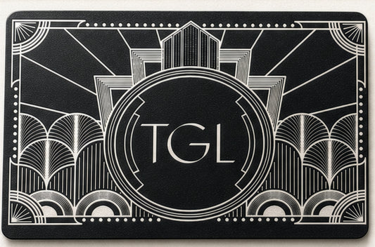 A black rectangular card or mat featuring an Art Deco style white line design with the letters 'TGL' centered inside a circular emblem.