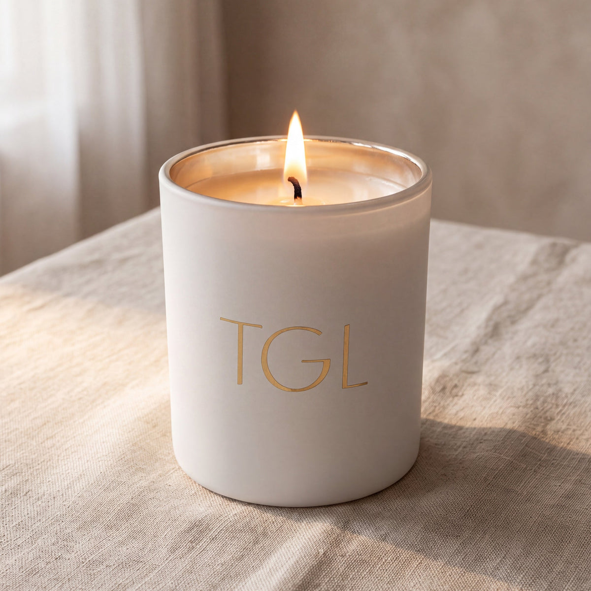 TGL soy candle by The GOOD LIFE, lit in a white jar on a linen draped table